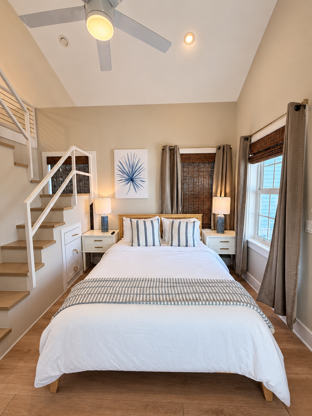 A neatly arranged bedroom with a bed, nightstands, lamps, and a staircase leading up.