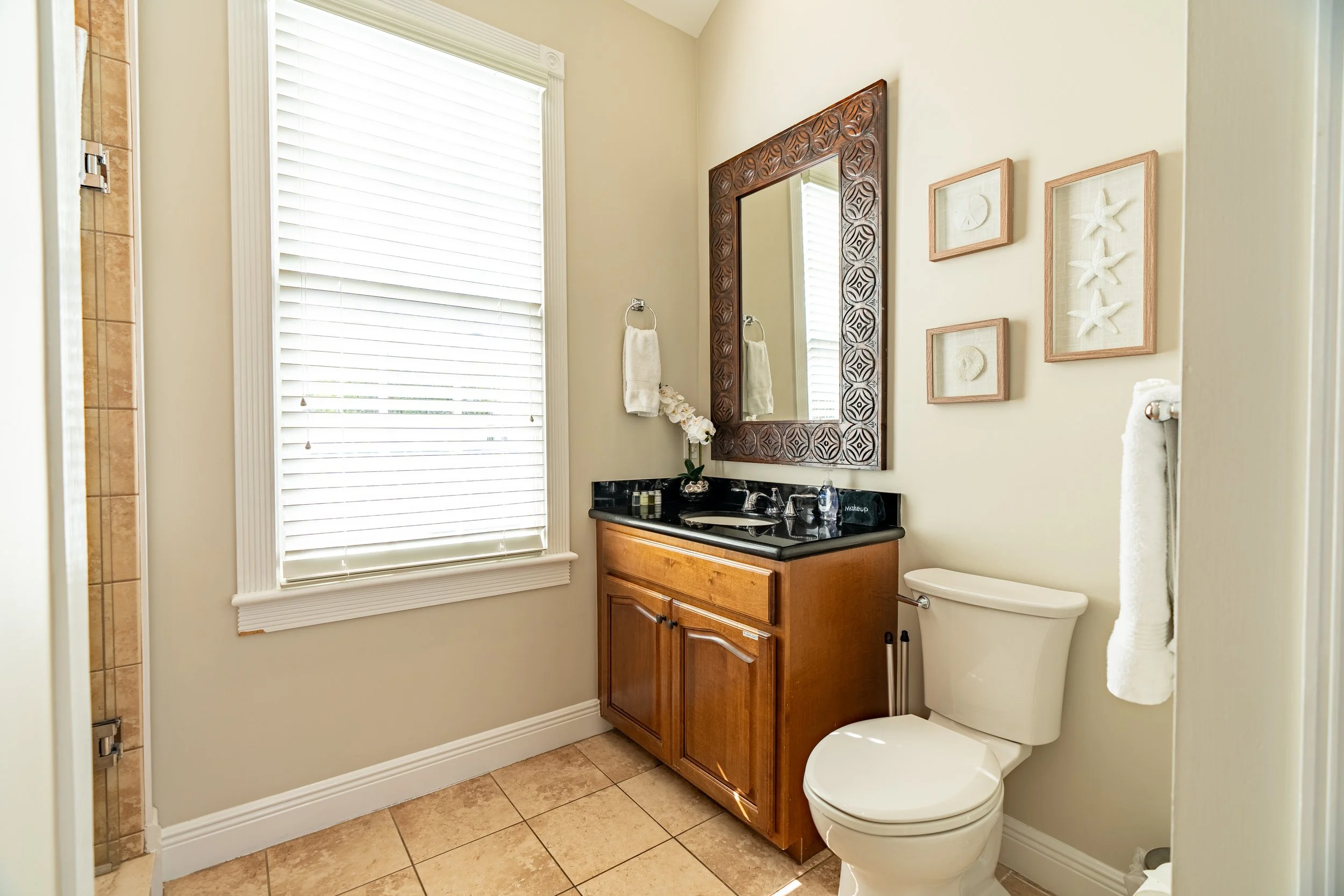 A clean bathroom with a wooden cabinet, black countertop, white toilet, and tiled floor.