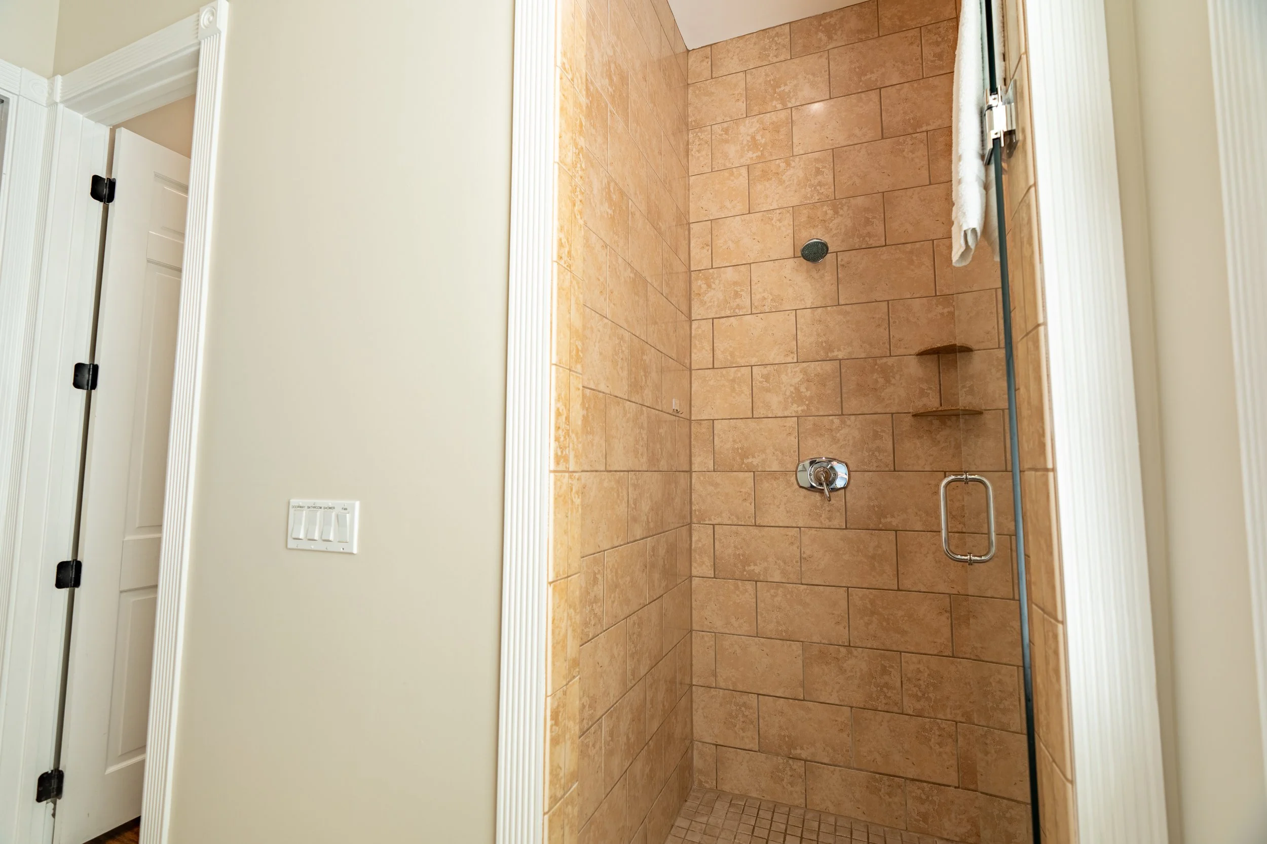 A tiled shower with a glass door and silver fixtures.
