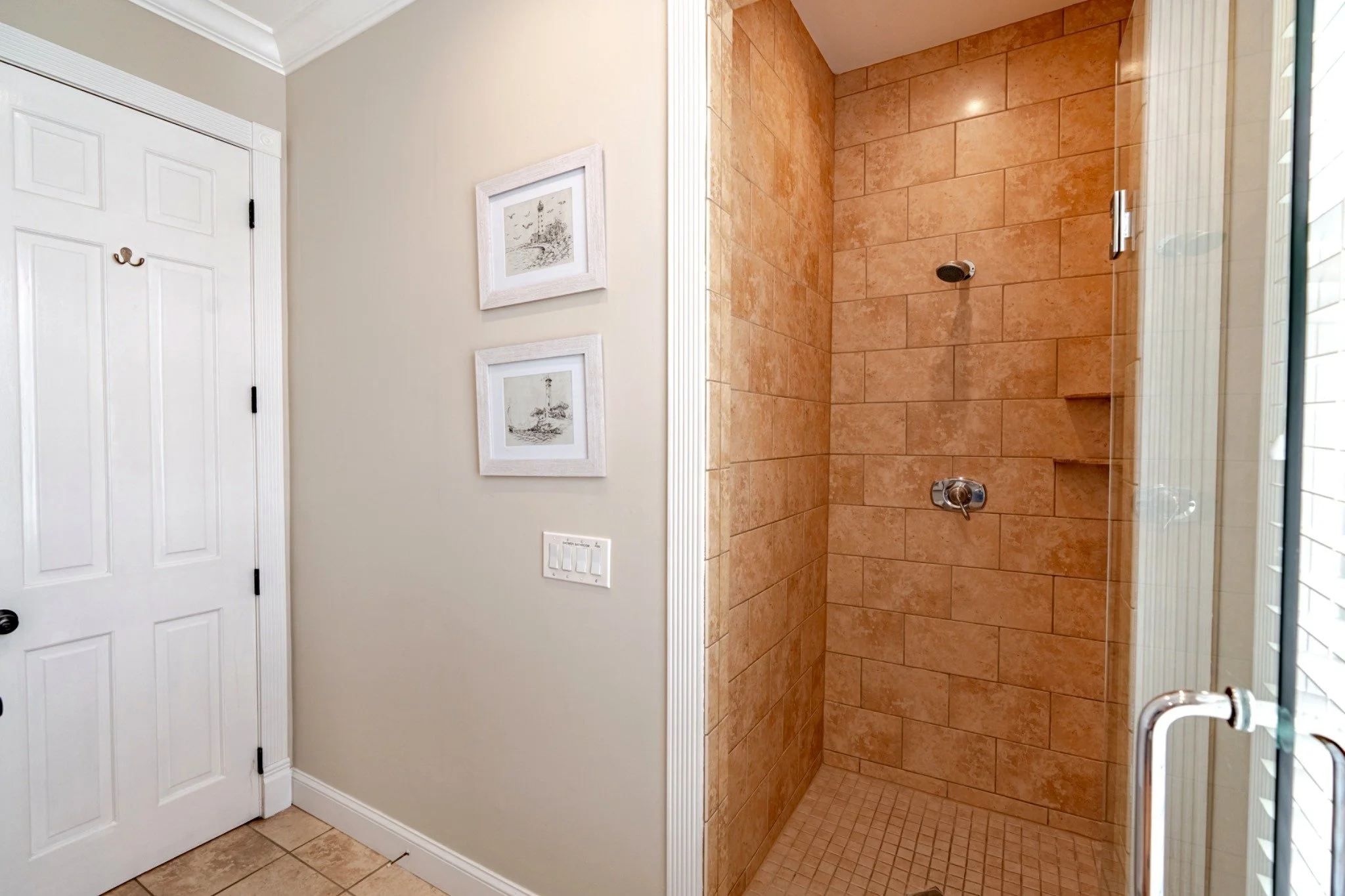 A bathroom with a tiled shower, glass door, and pictures on the wall.