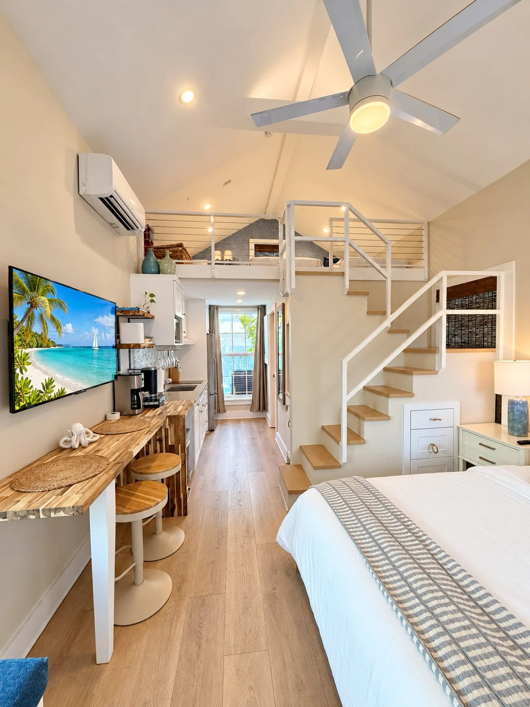 A compact hotel room with a kitchenette, loft bed, and staircase.