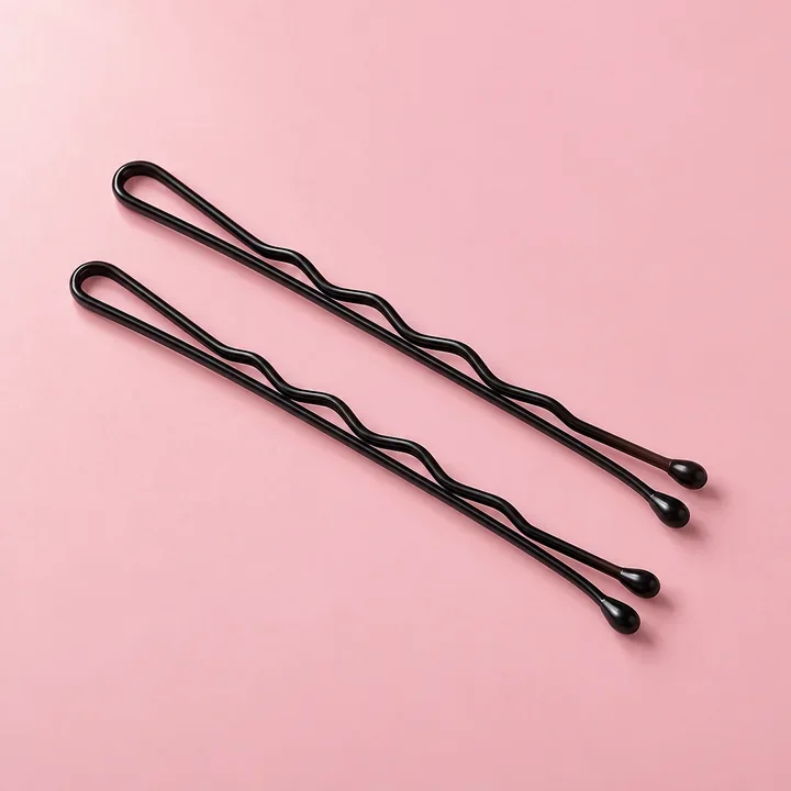 Two black bobby pins on a blush surface. Illustrative product concept.
