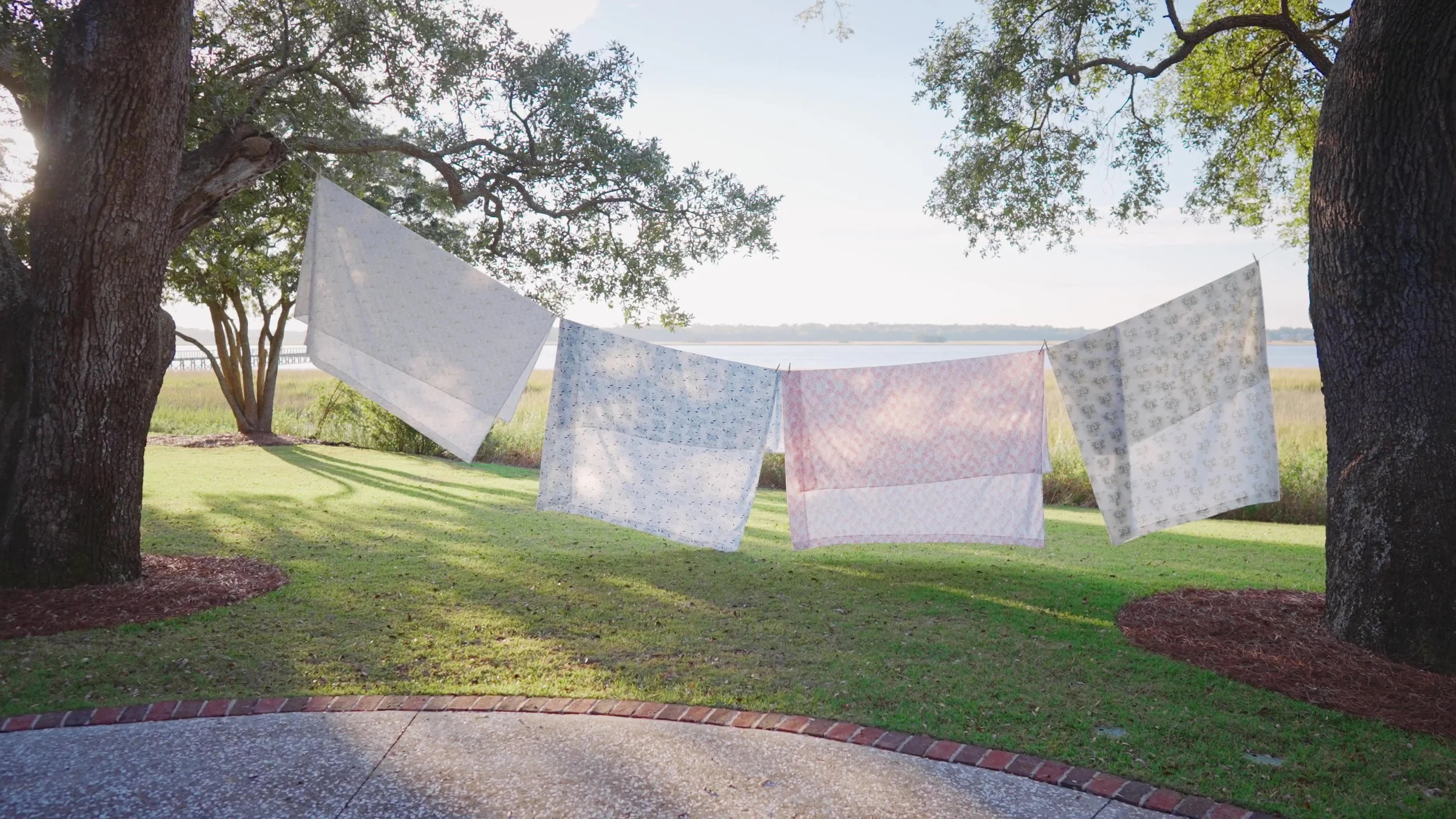 Patterned textiles hanging between oak trees beside the water