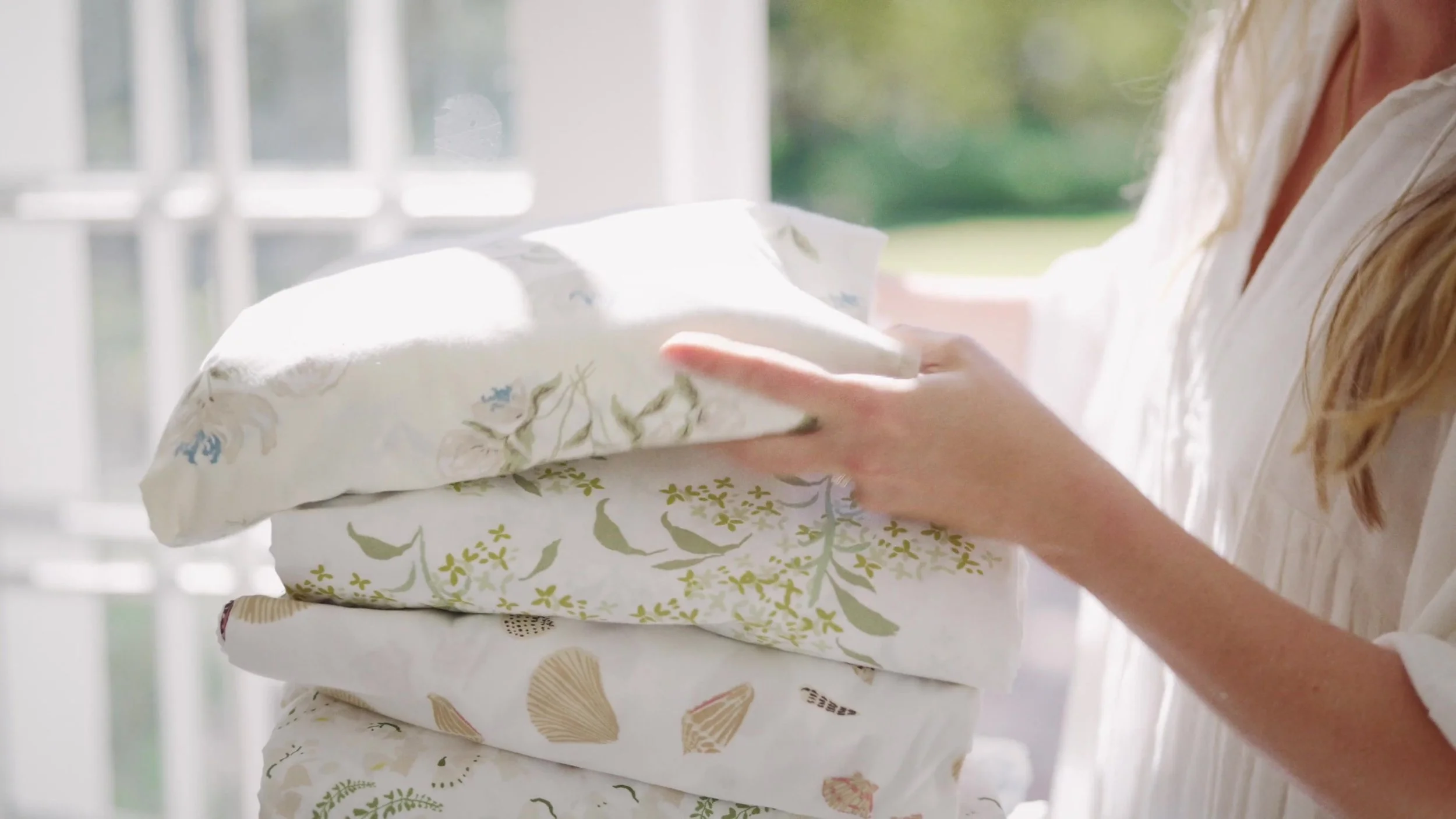 Hands arranging a stack of botanical and shell-patterned textiles