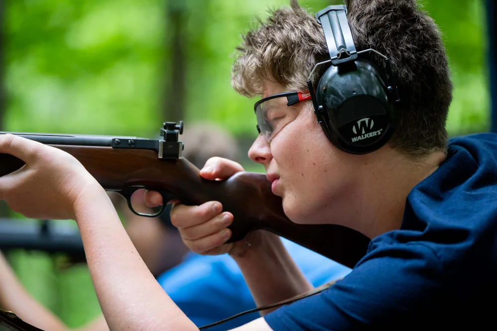 Boy aiming rifle at target in a forest