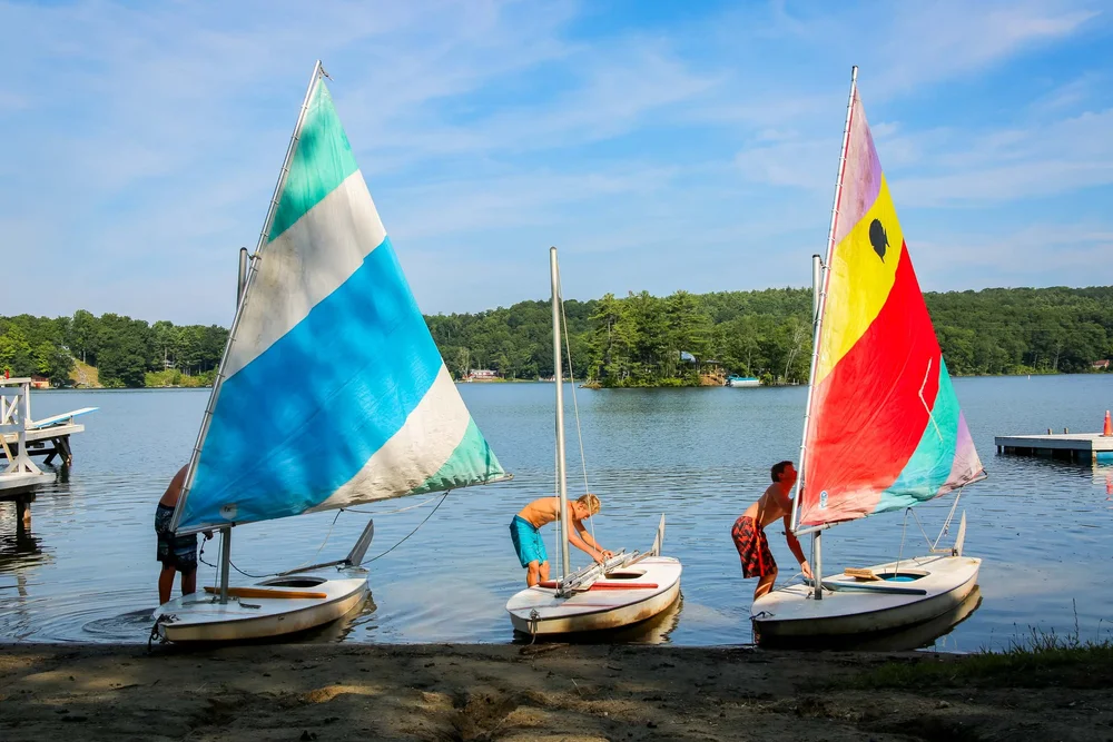 Campers preparing colorful sailboats on the shore