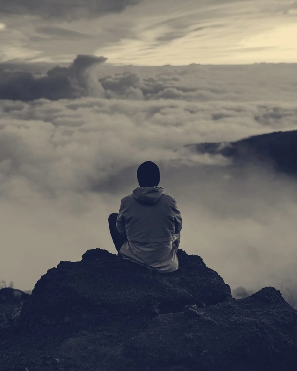 A person sitting on a mountaintop above a sea of clouds at sunset