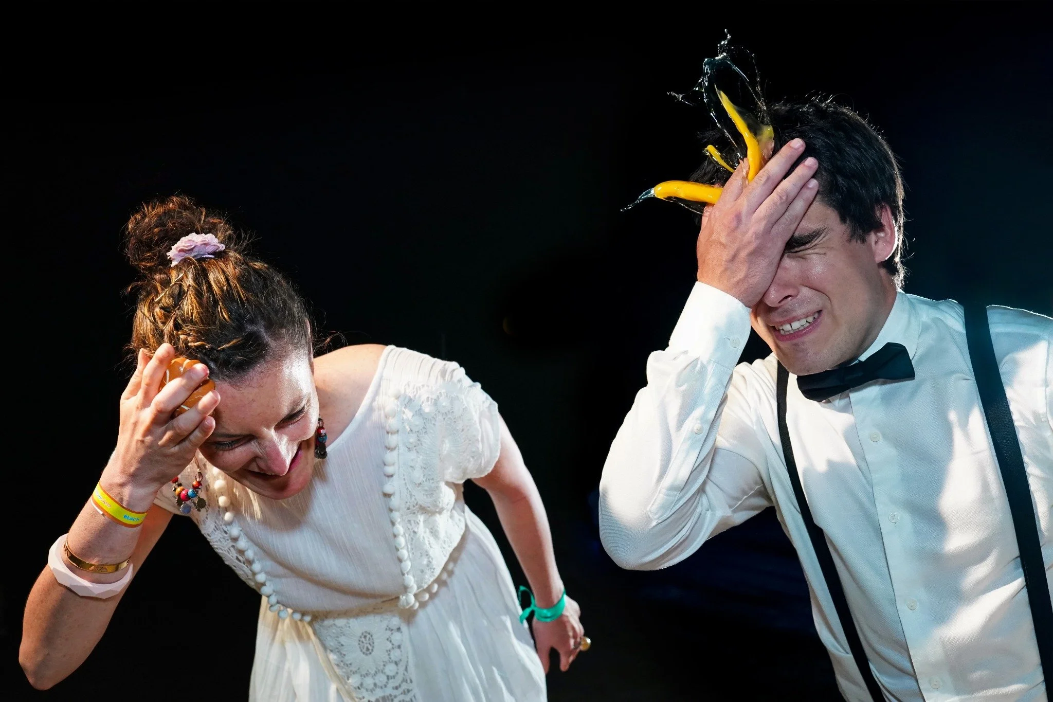 A bride and groom laugh and wince as eggs break against their foreheads during a wedding game.