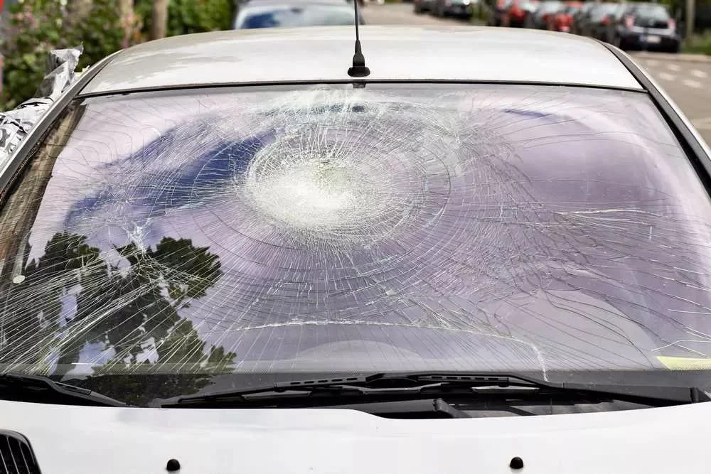 Pare-brise d'une voiture blanche étoilé par un choc, avec des fissures sur toute la surface