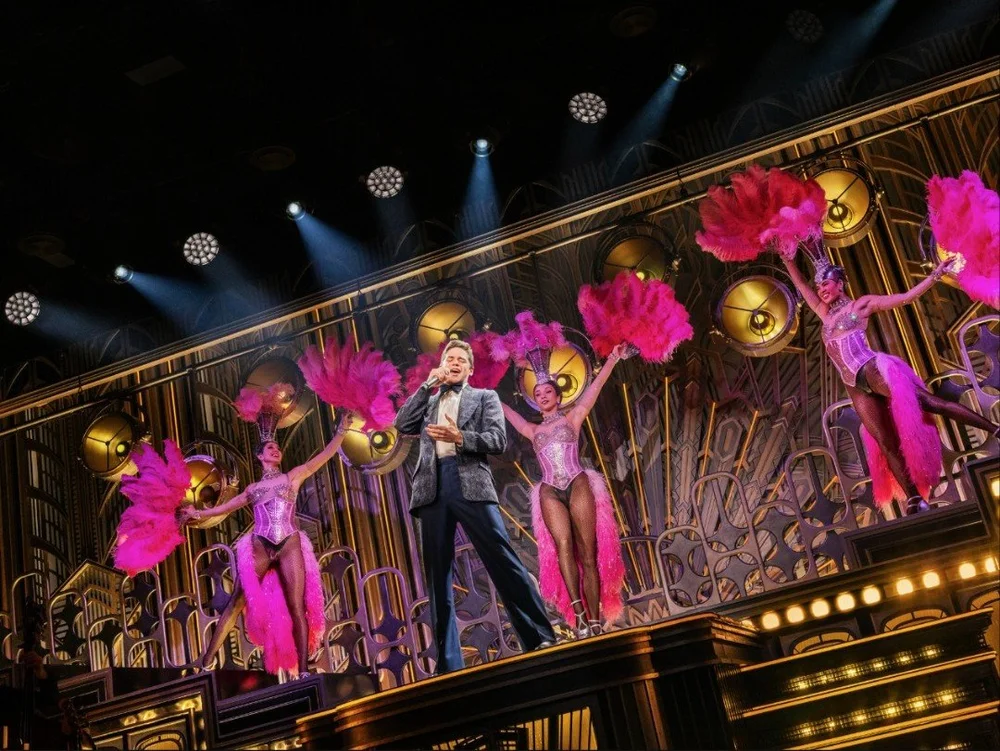 Jeremy Jordan as Bobby Darin, flanked by showgirls with pink feather fans, in Just in Time on Broadway