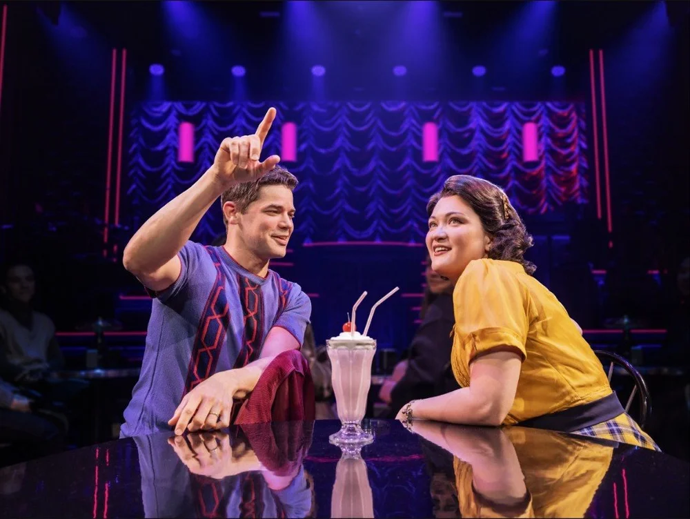 Jeremy Jordan as Bobby Darin and Isa Briones as Connie Francis share a milkshake at a diner counter in Just in Time