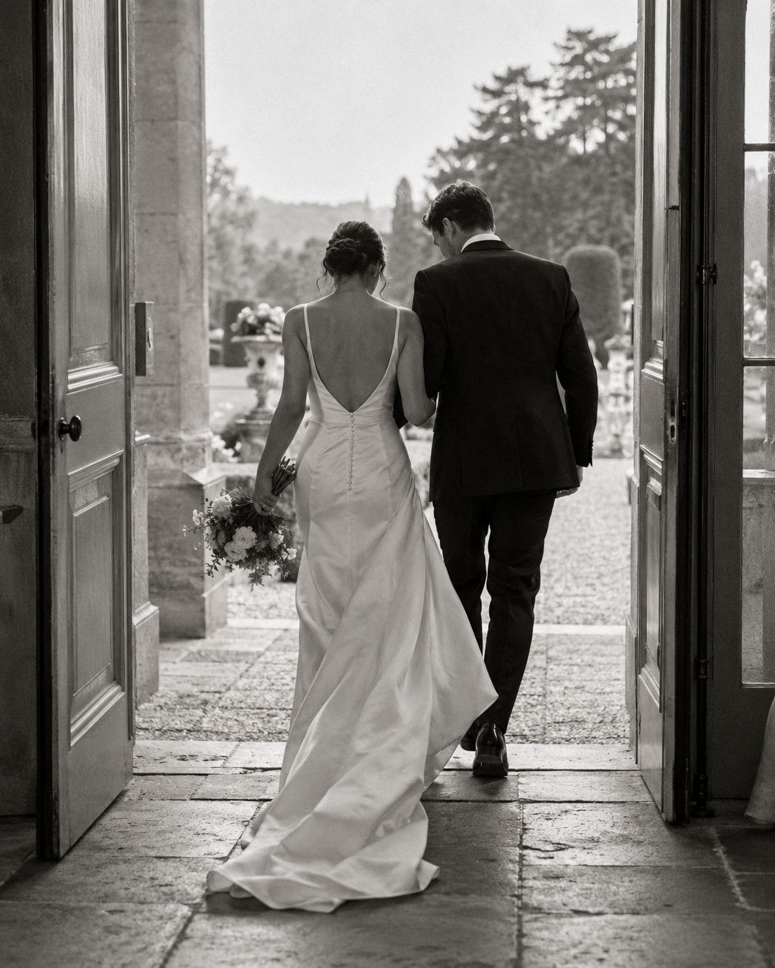 Black-and-white portrait of a couple walking into a country-house garden