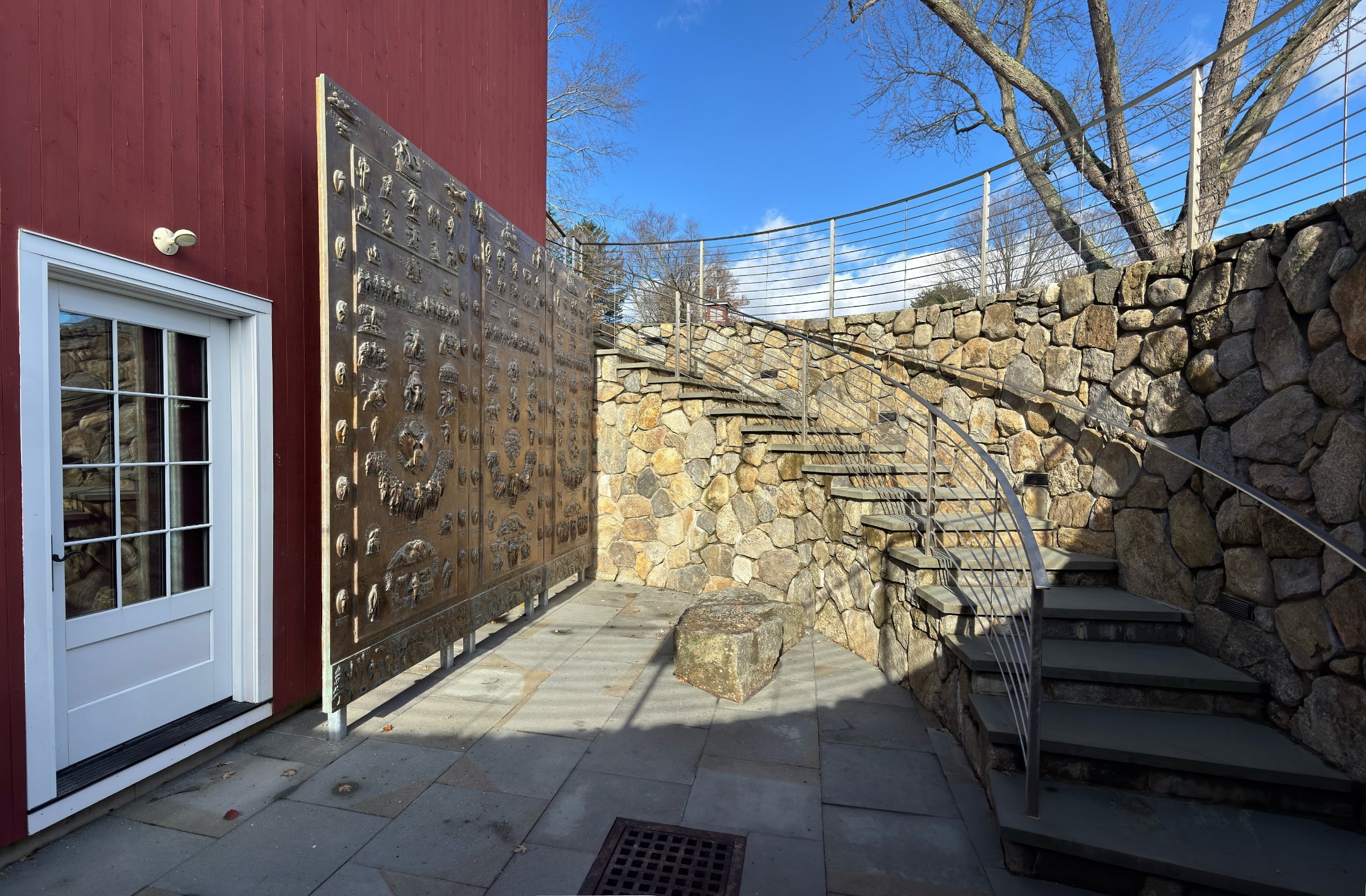 The three bronze Fraser Panels standing side by side in the stone-walled stairwell of the Visitor Center, beside a curved stone stair.