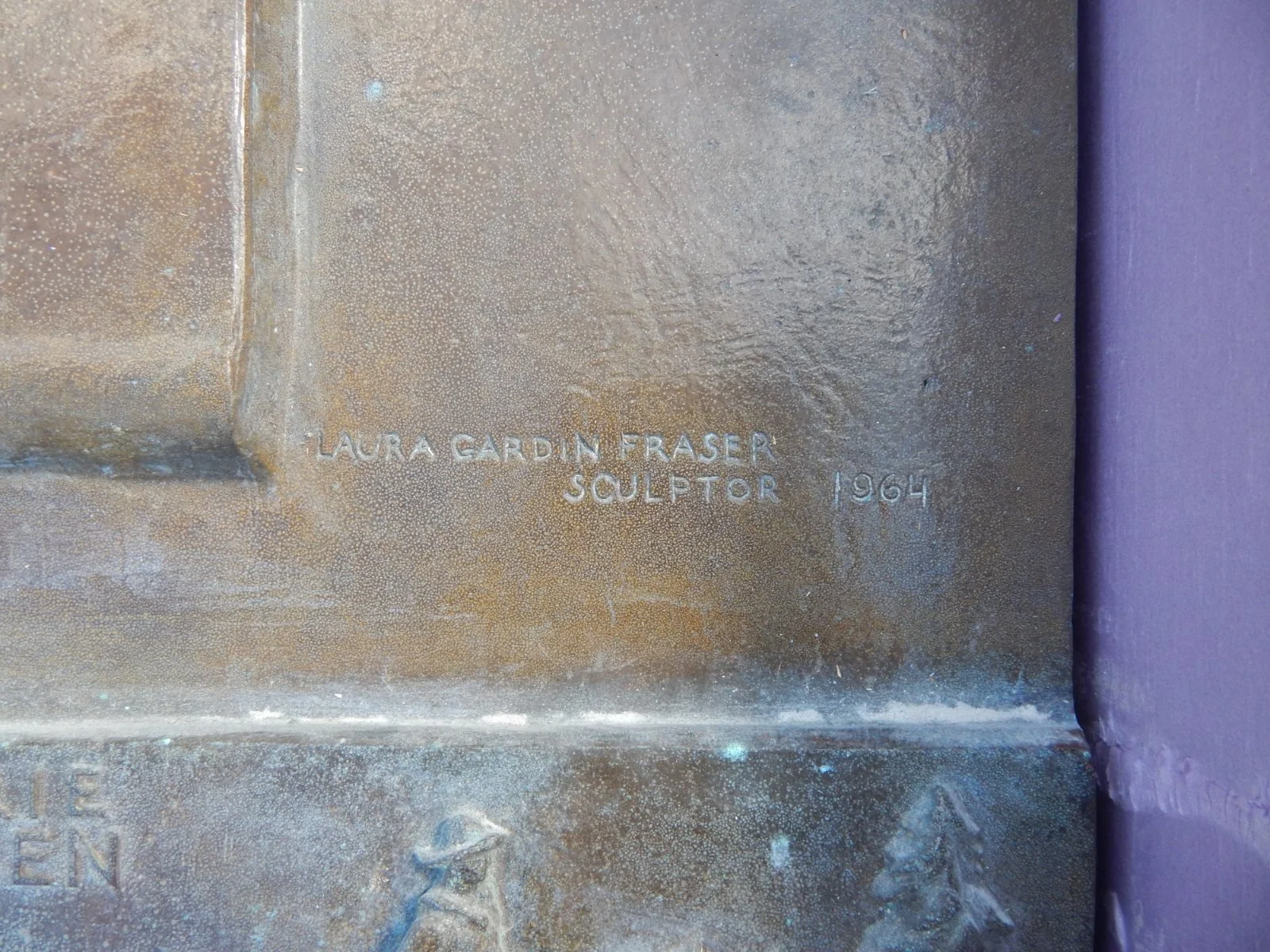 Close-up of the bronze's edge, where the words Laura Gardin Fraser, Sculptor, 1964 are cut into the metal.