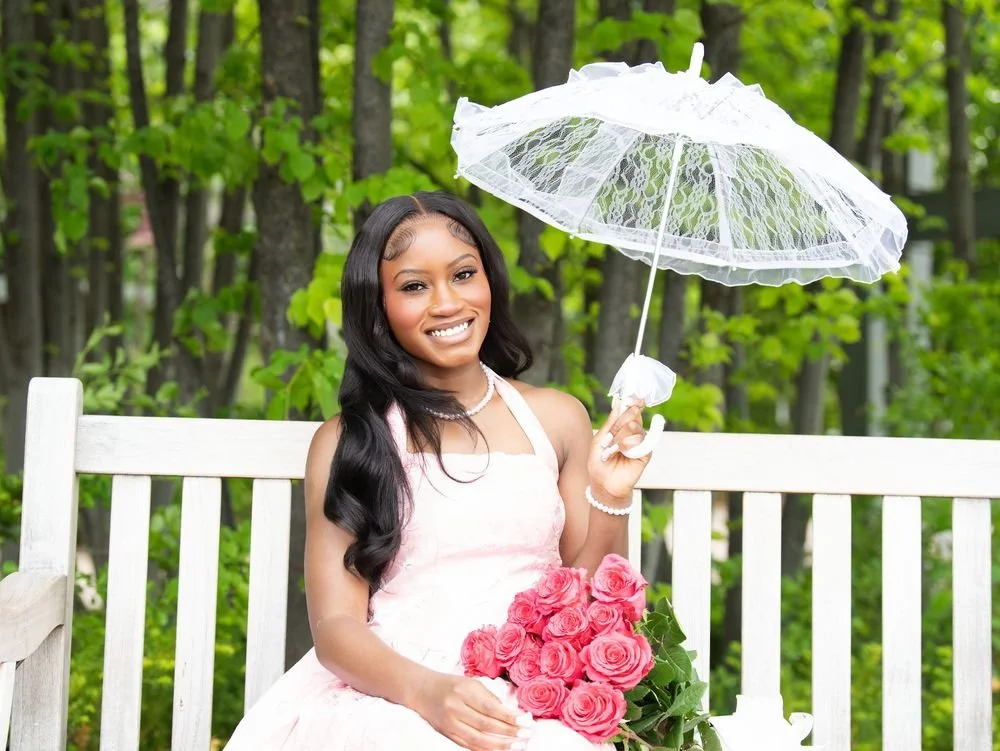A young woman in a pink dress holding roses and a lace parasol on a garden bench