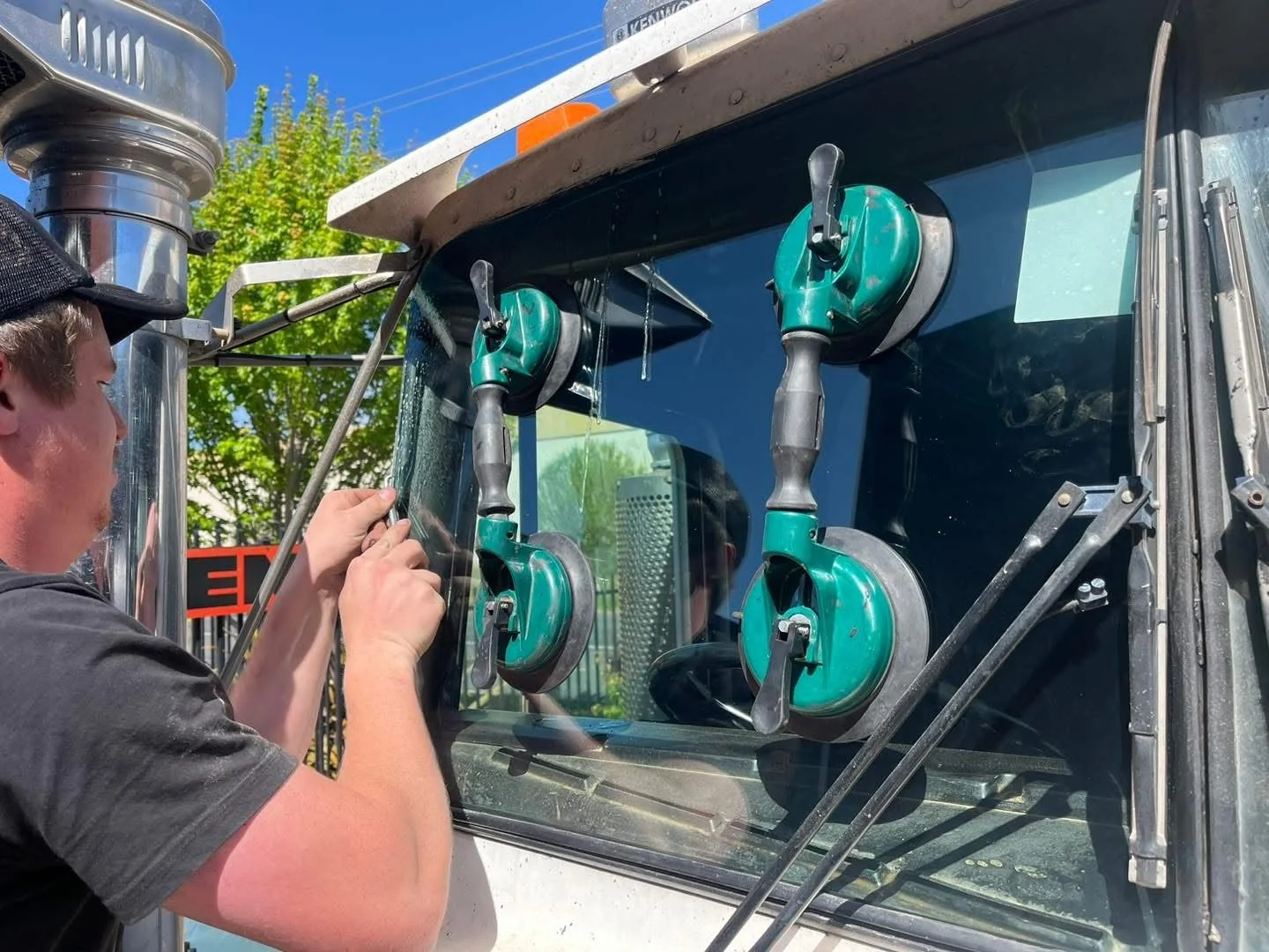 Orange Auto Glass technician lifting a windscreen into place with suction cups