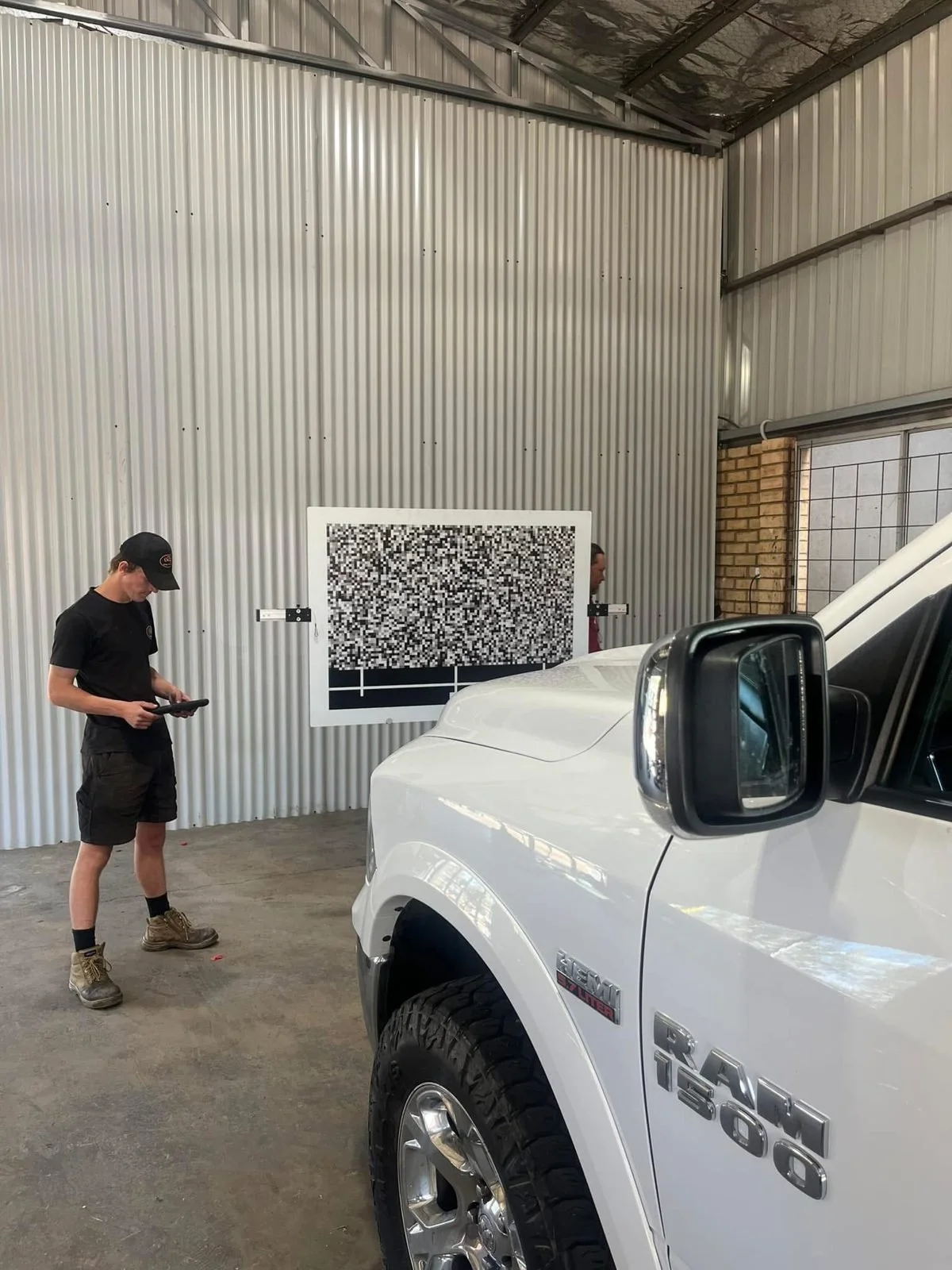 Technician recalibrating the forward-facing camera on a RAM 1500 using a calibration target board in the Orange Auto Glass workshop