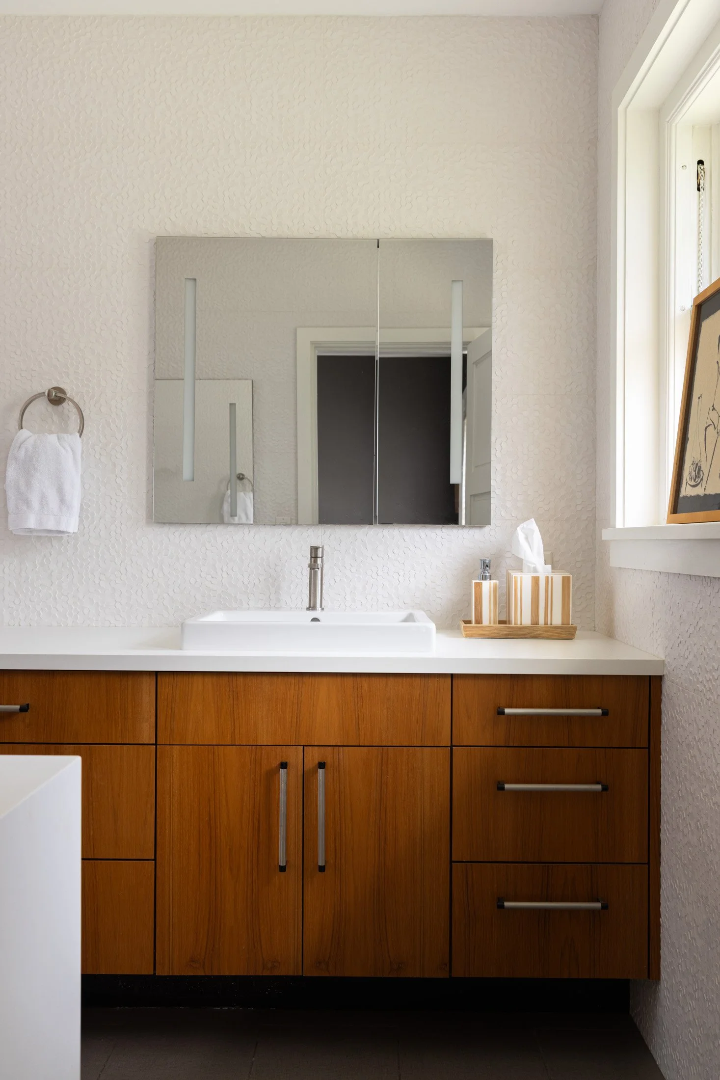 Bathroom vanity with warm wood cabinetry and a rectangular mirror