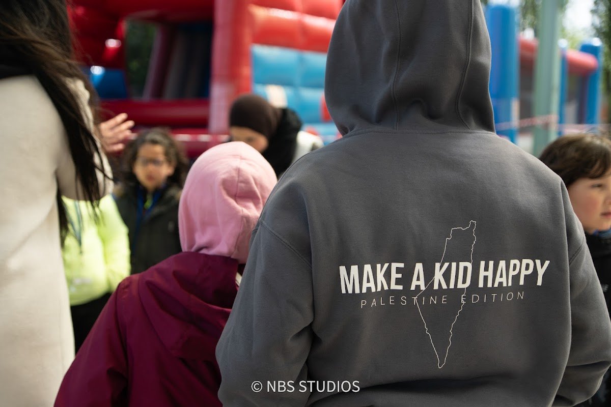 A volunteer in a Make A Kid Happy hoodie among the children