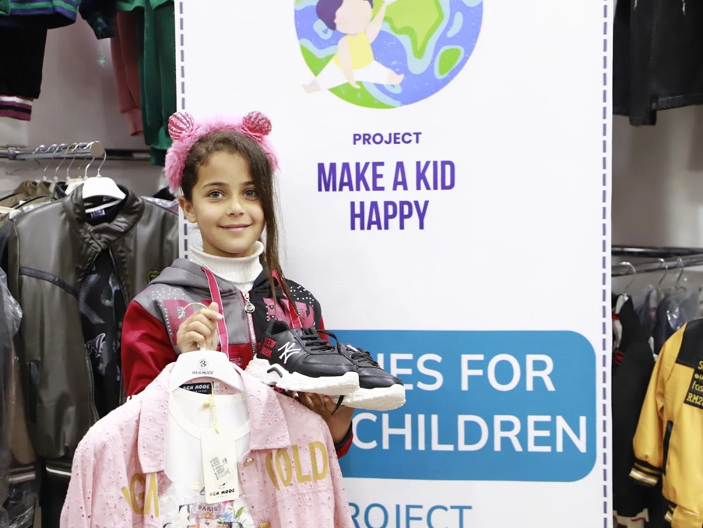 A girl holding new clothes and shoes from the Clothes for Children project