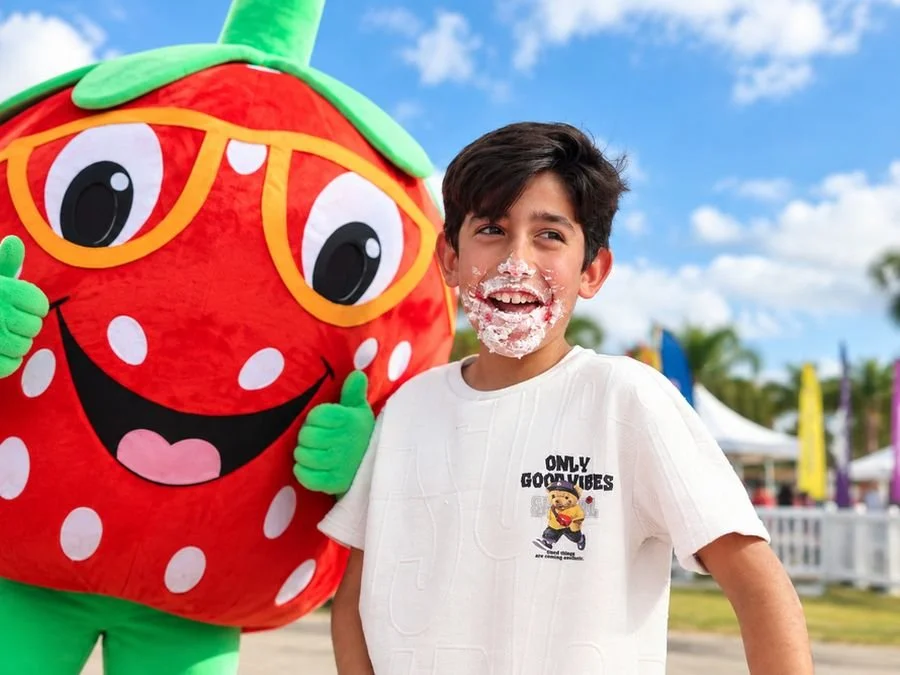 Smiling boy with whipped cream on his face next to the strawberry mascot