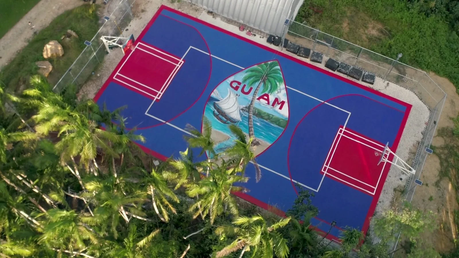 Aerial view of a basketball court painted with the Guam seal, framed by trees