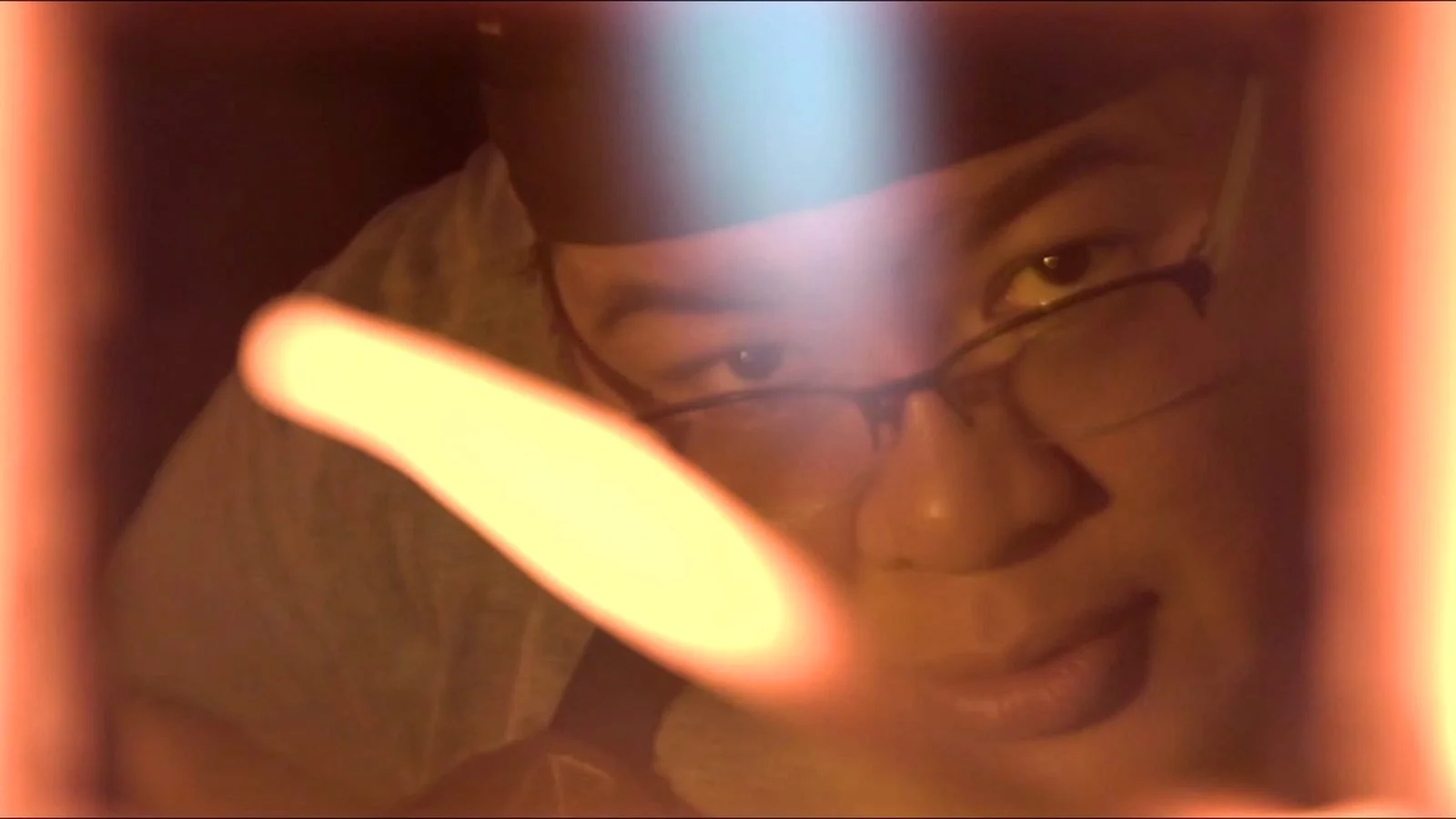 A woman in glasses looks through a warm streak of light