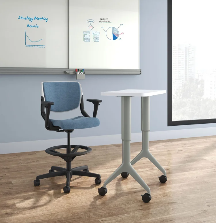 Upholstered task stool beside a mobile standing table