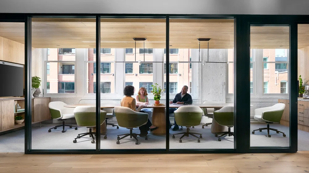 Glass-walled meeting room with green and cream lounge chairs