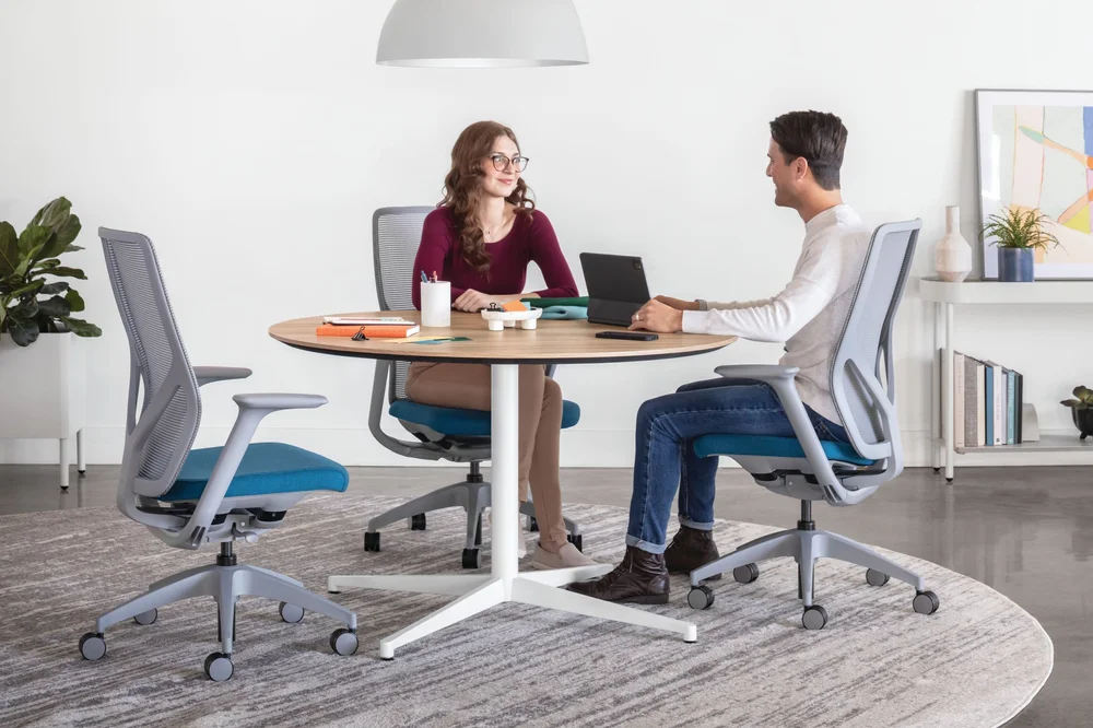 Two colleagues meeting at a round table in mesh task chairs