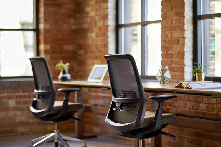 Black mesh task chairs at desks by a brick wall