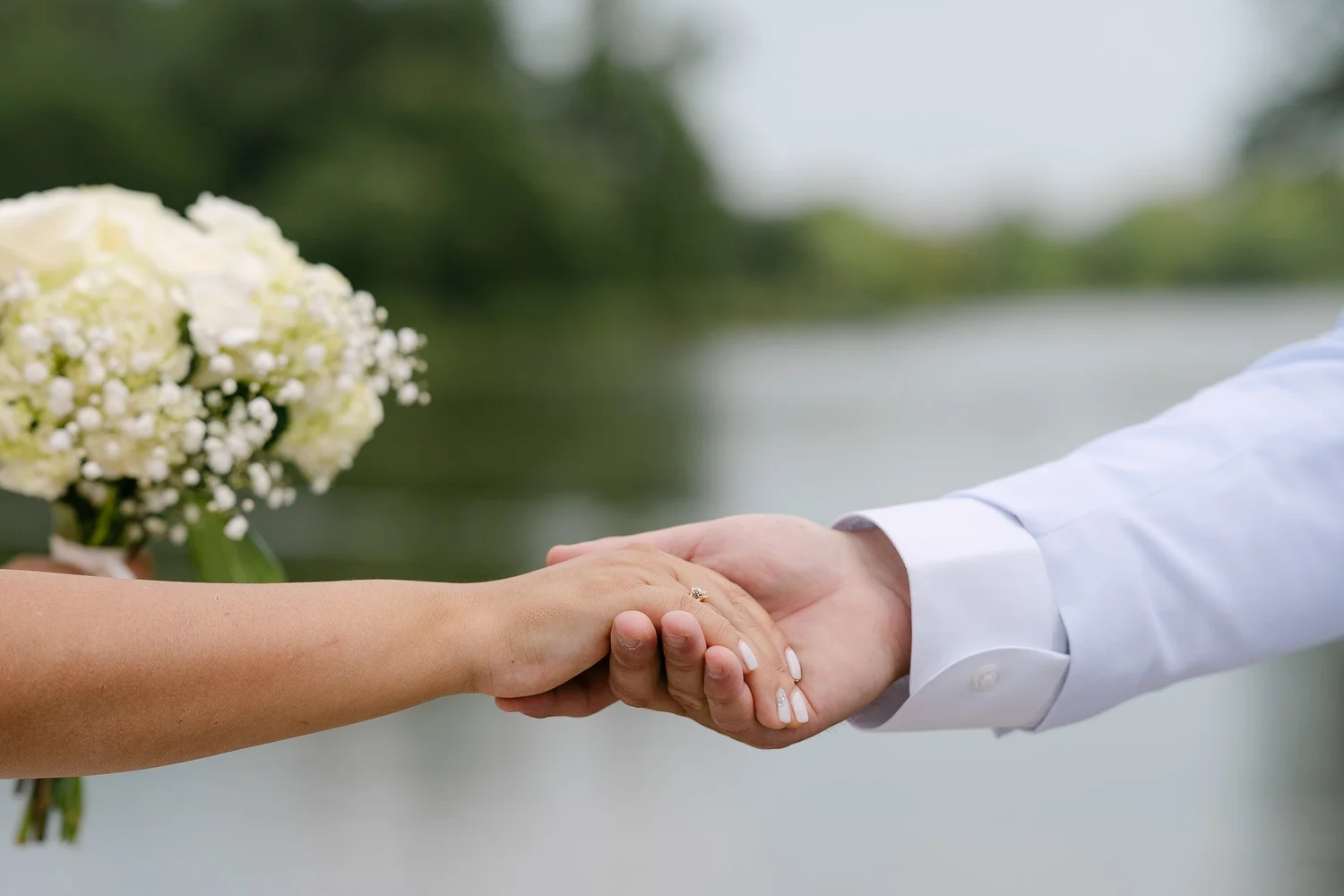 Couple holding hands with a bouquet by the lake