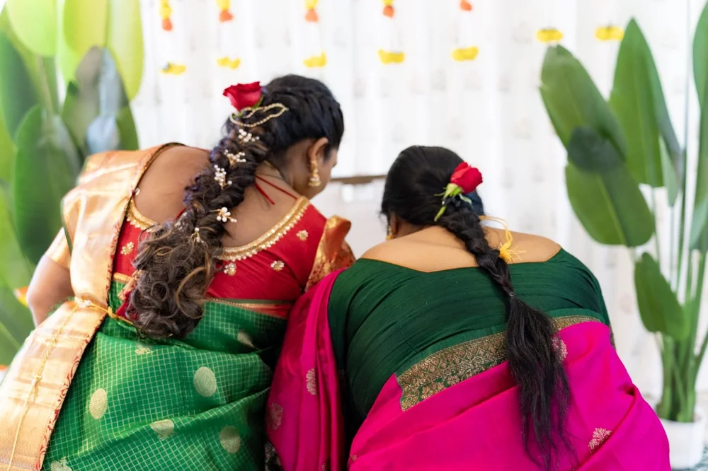 Two women in silk saris with jasmine-braided hair at a ceremony