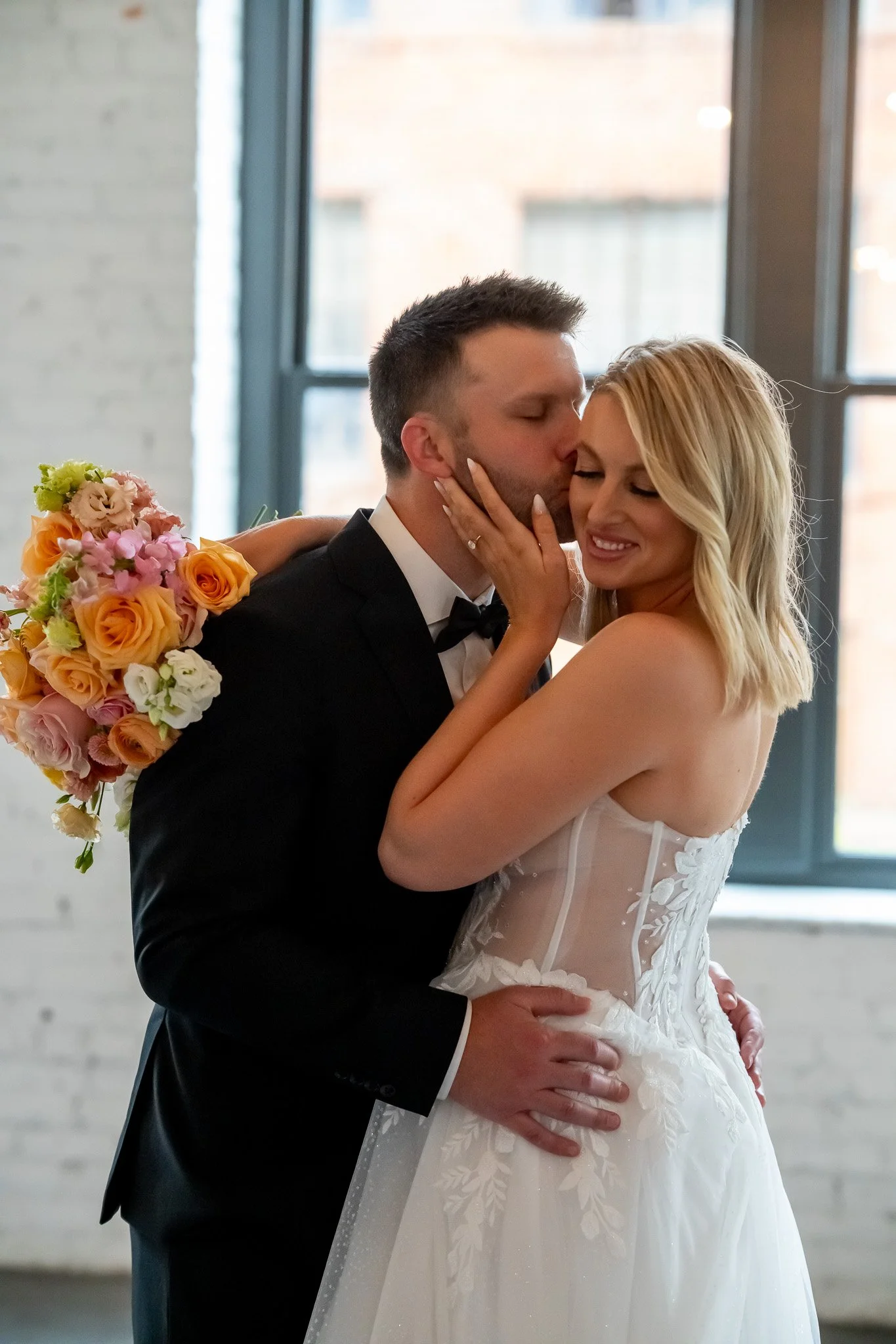 Bride and groom embracing with a peach bouquet