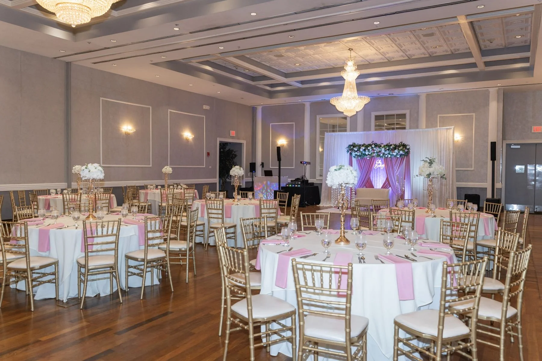 A chandelier-lit ballroom set with gold chairs and a floral stage