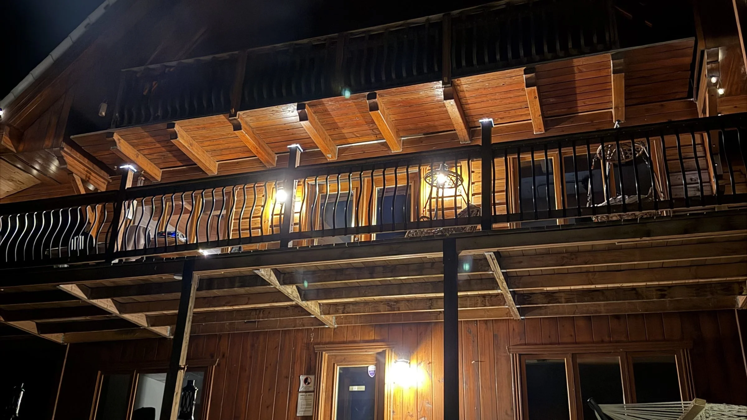 Le chalet Hopelaï illuminé le soir, avec sa grande galerie en bois