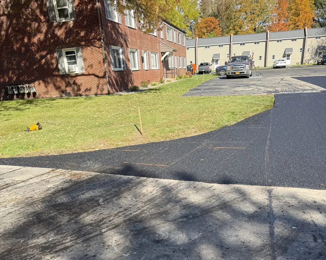 New asphalt repair along a lawn edge beside a brick building