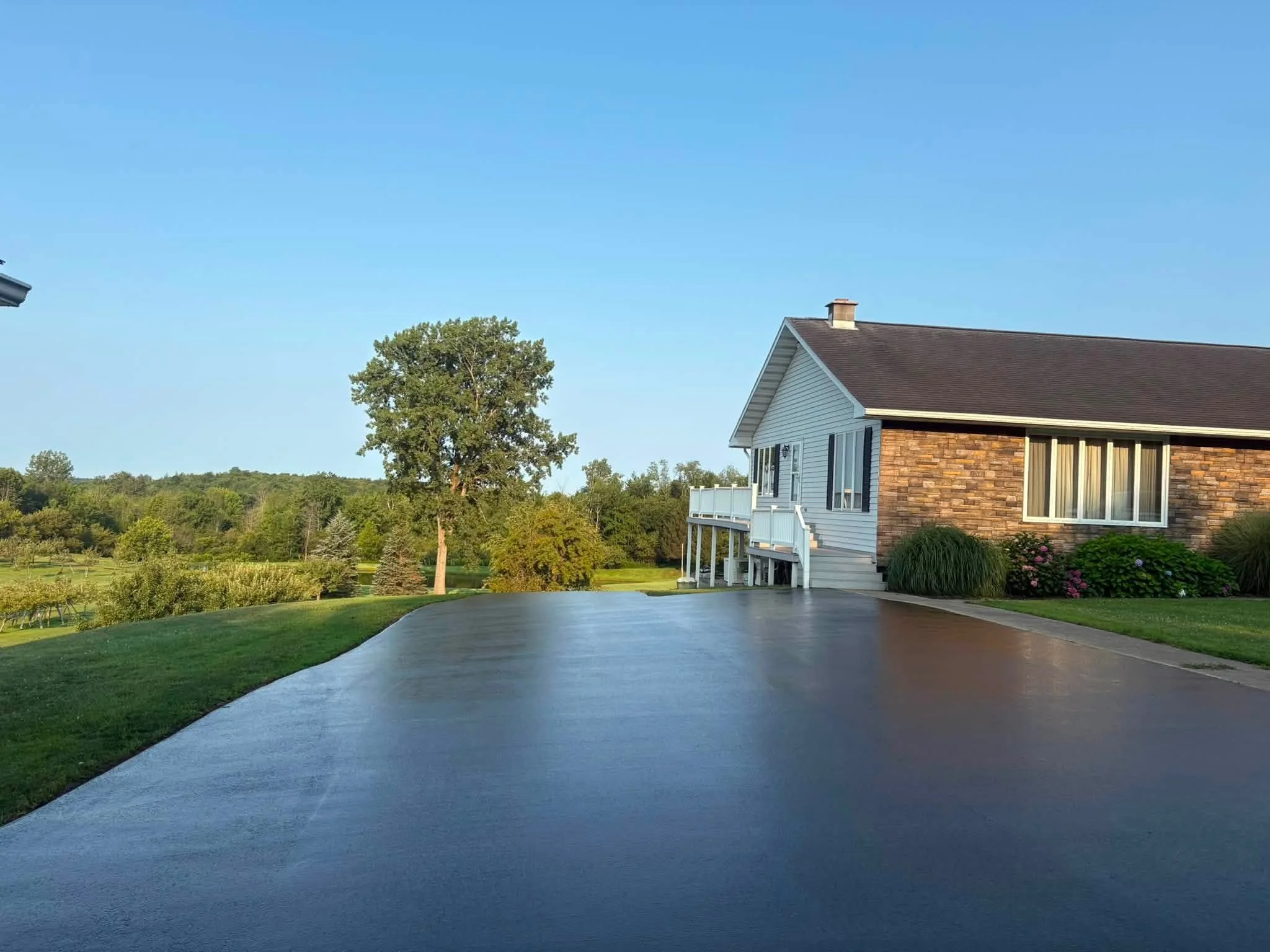 Freshly sealcoated driveway beside a brick and siding home