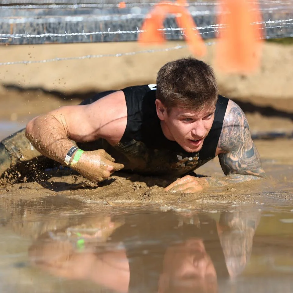 Daniel crawling through a muddy obstacle course