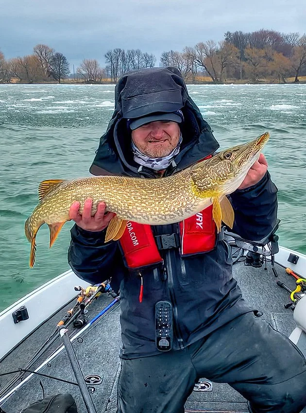 Pete Bowman holding a Northern Pike with ice in the background