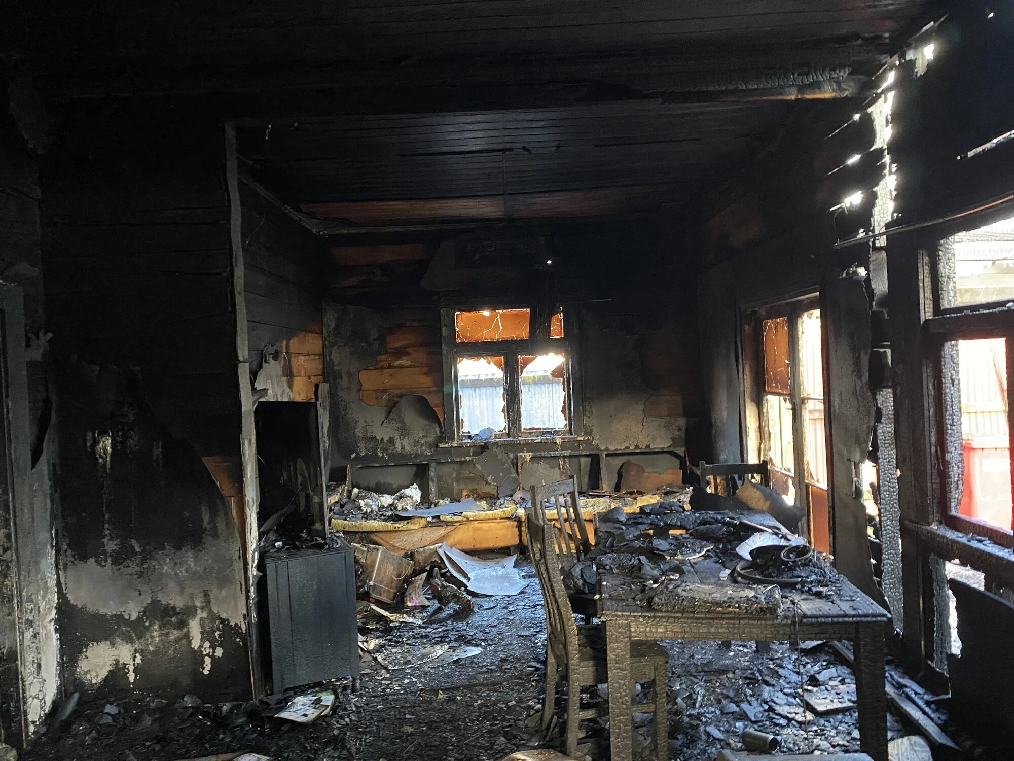 Living room with fire and smoke damage, charred furniture and soot-covered walls
