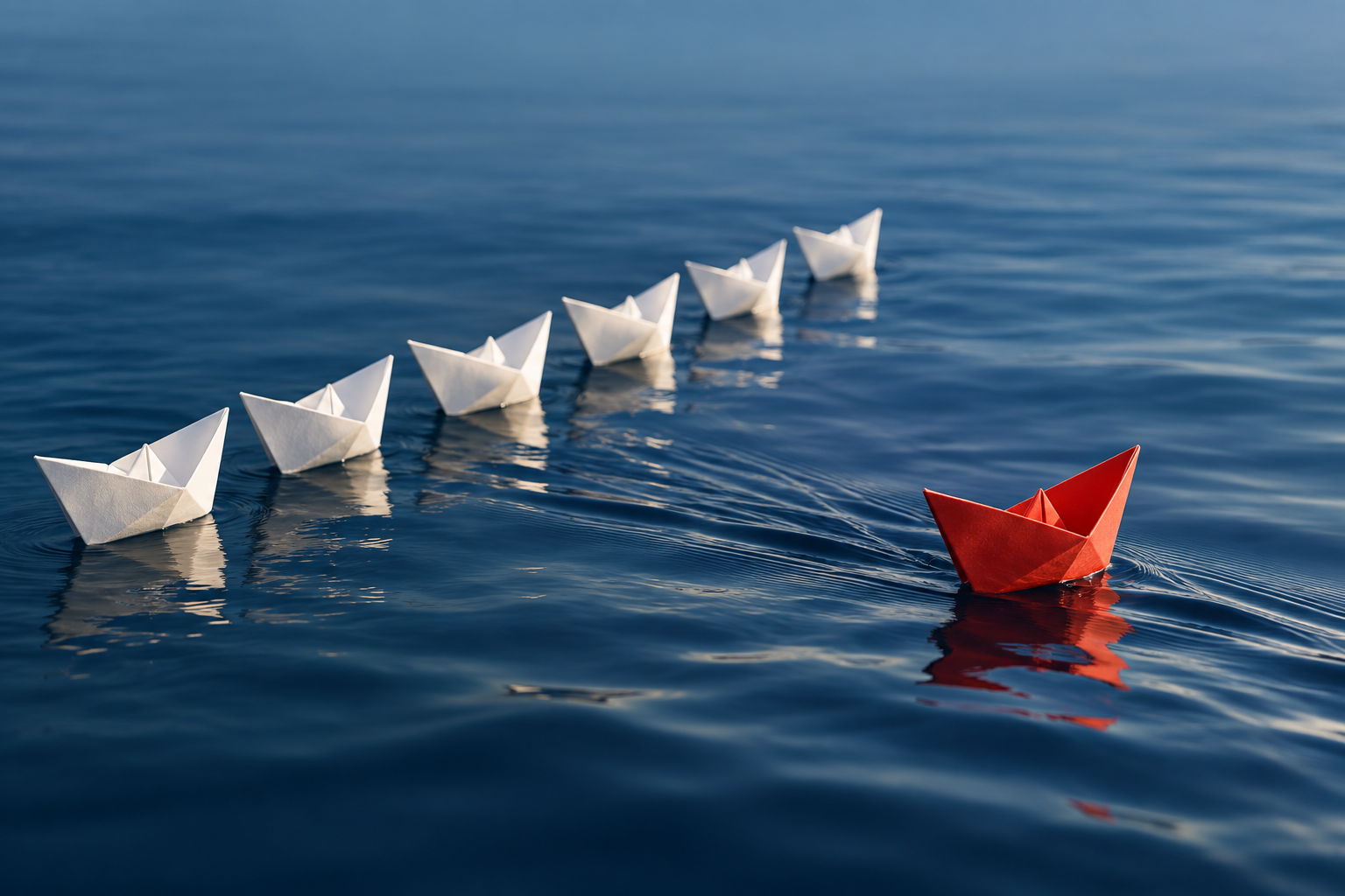 A red paperboat sailing on its own course away from a straight, orderly line of white paperboats on blue water.