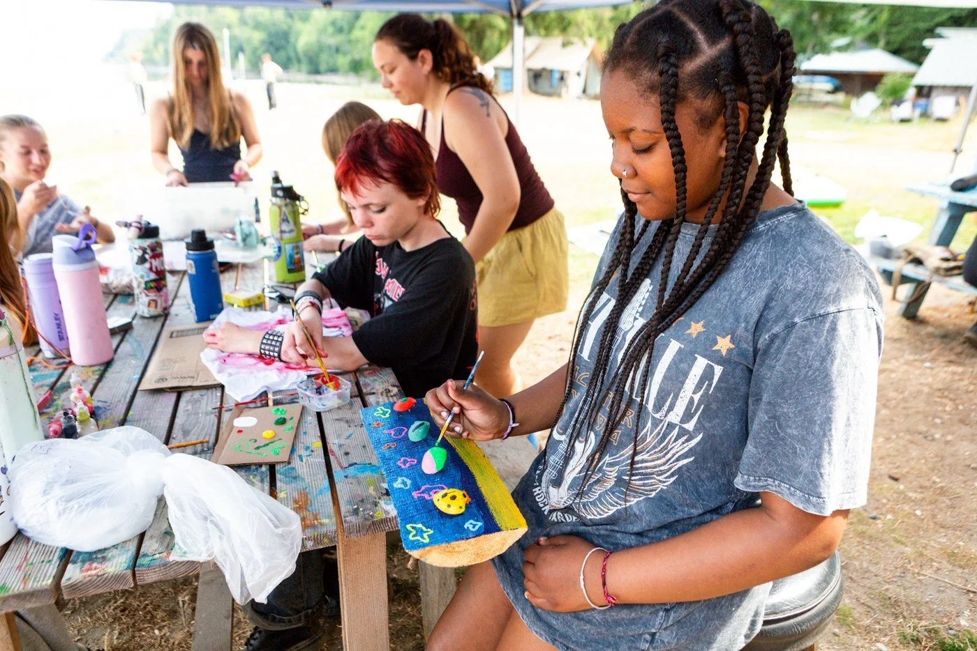 Campers painting at a picnic table under a canopy at Camp