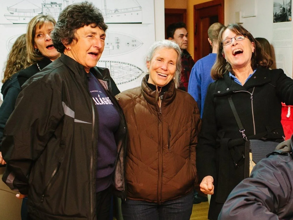Three women laughing and singing at the kickoff event, one wearing a Gallagher sweatshirt