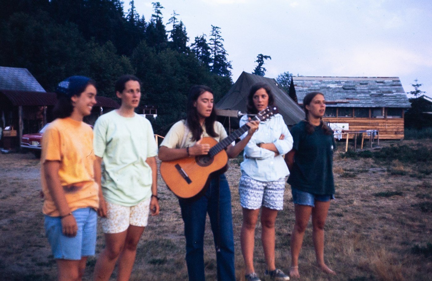 Five young women singing together at Camp in 1970, one playing a guitar
