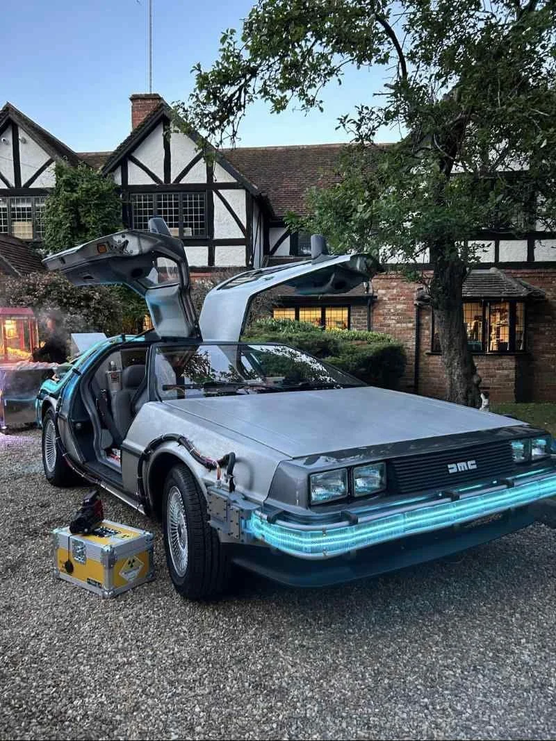 Movie replica time machine with gull-wings open outside a Tudor house