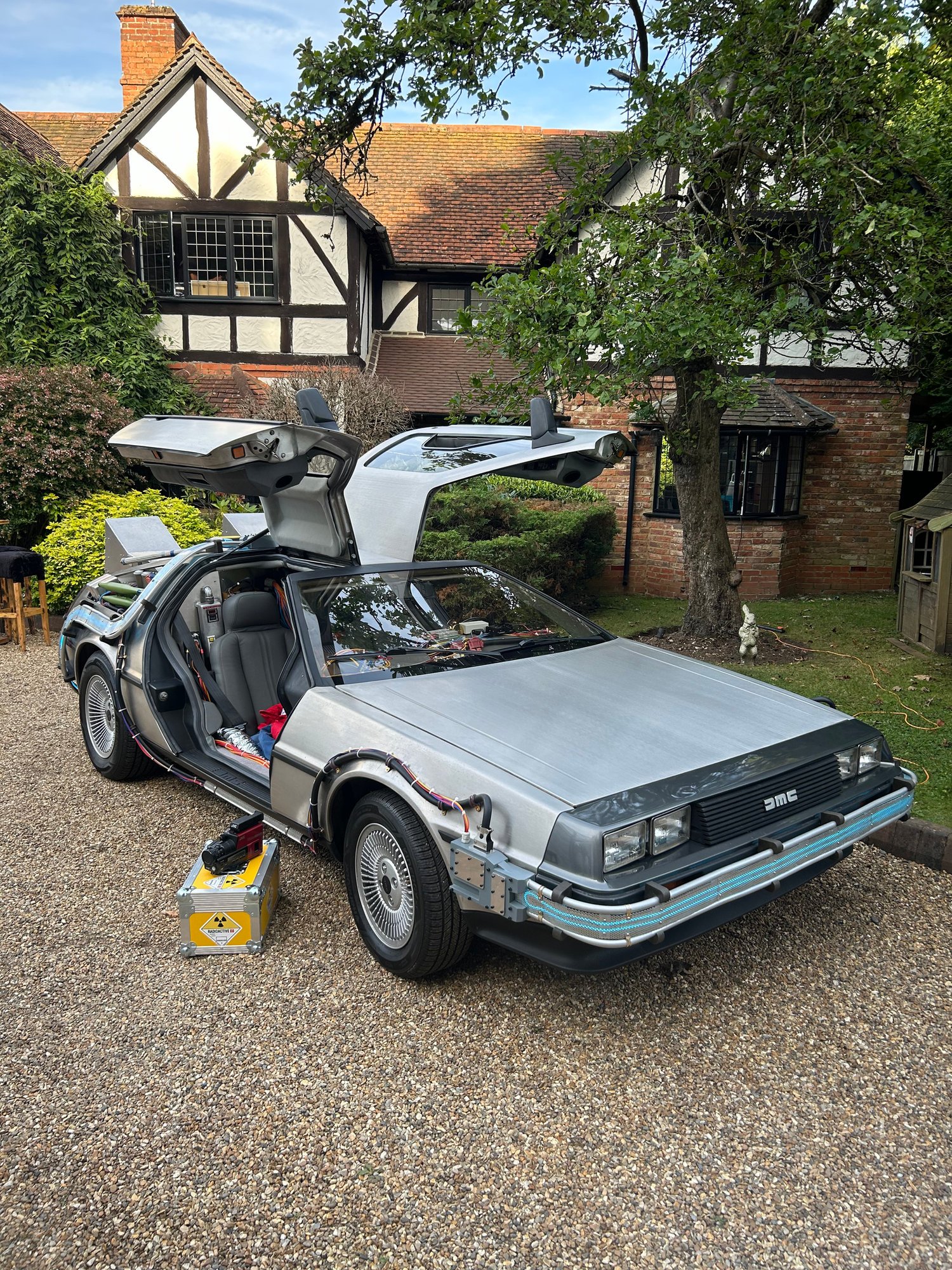 Time machine with gull-wing doors open outside a Tudor house