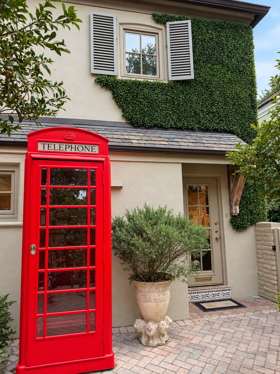 Climbing boxwood greenwall framing the upper window of a Coral Gables home, with a red telephone booth and potted olive in the front courtyard