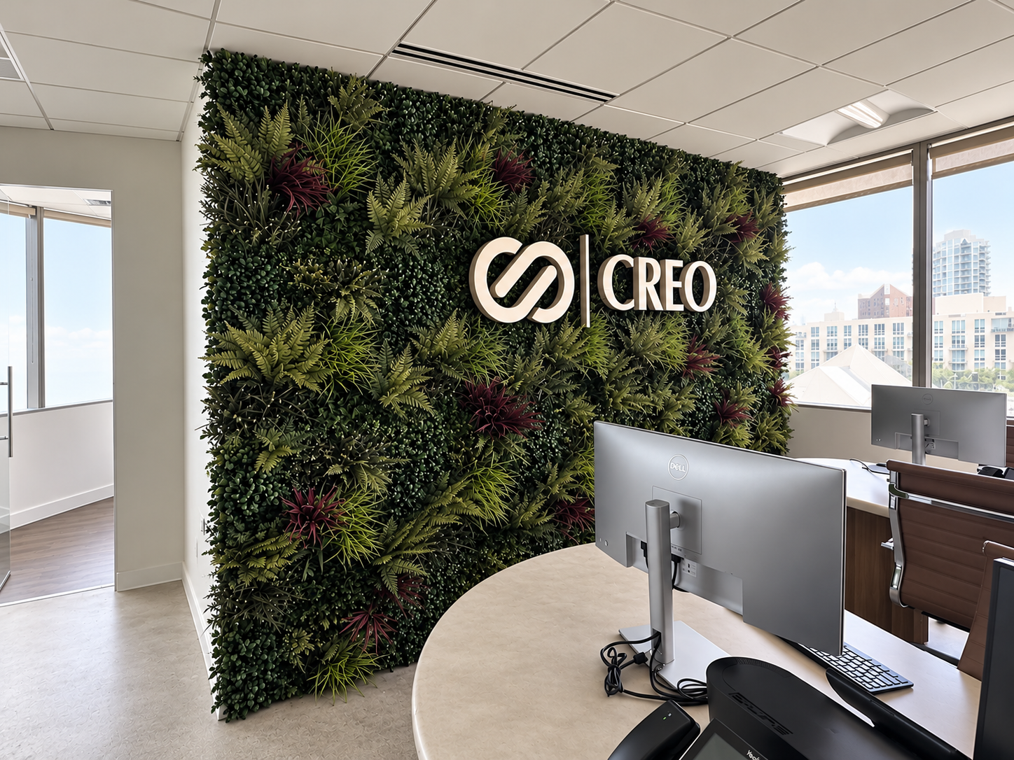 Floor-to-ceiling artificial greenwall with ferns and burgundy accents framing an illuminated company logo in a corporate office