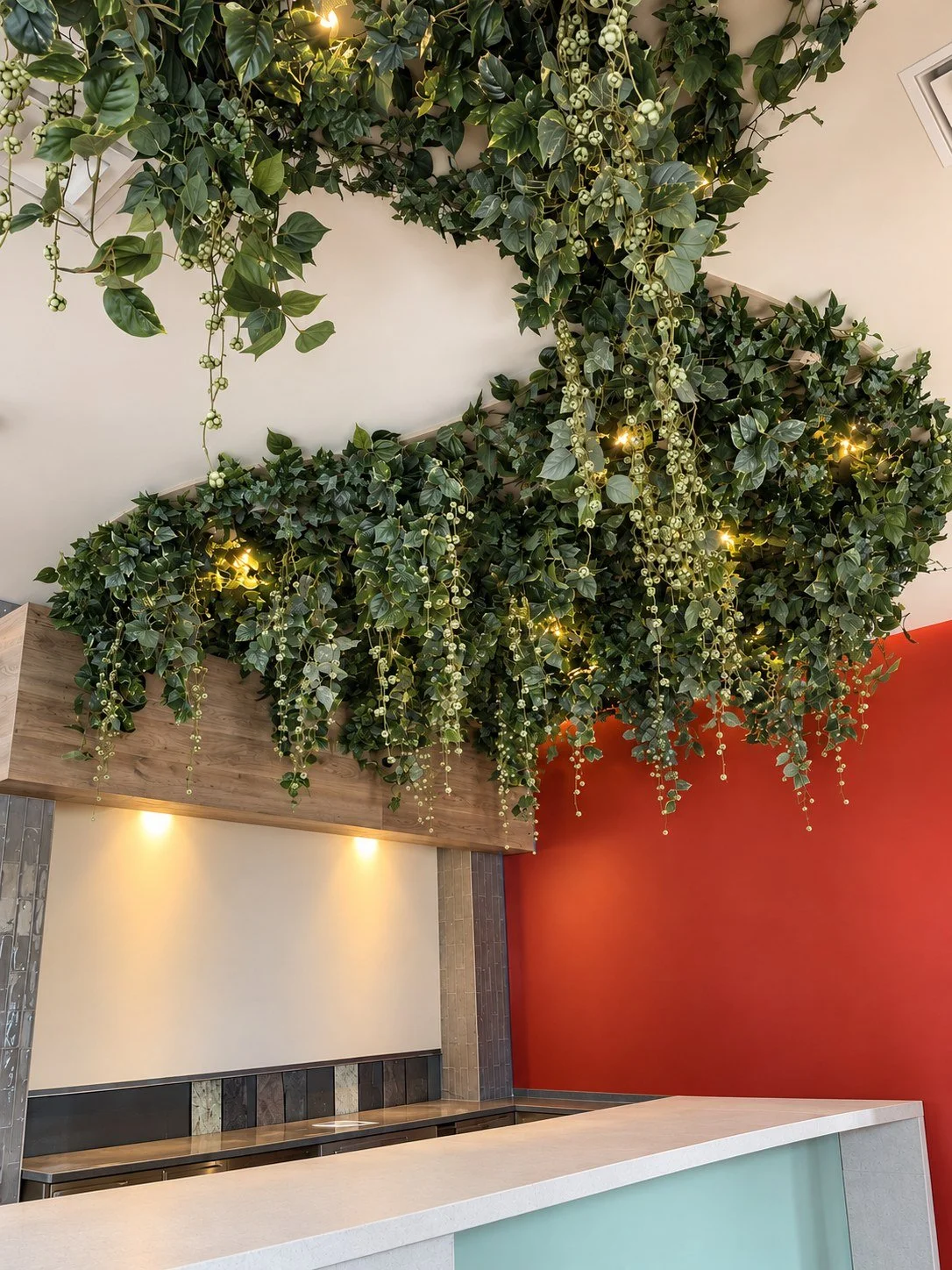 Artificial ivy and berry vines cascading from a restaurant ceiling over the bar, with warm string lights, in Fort Lauderdale